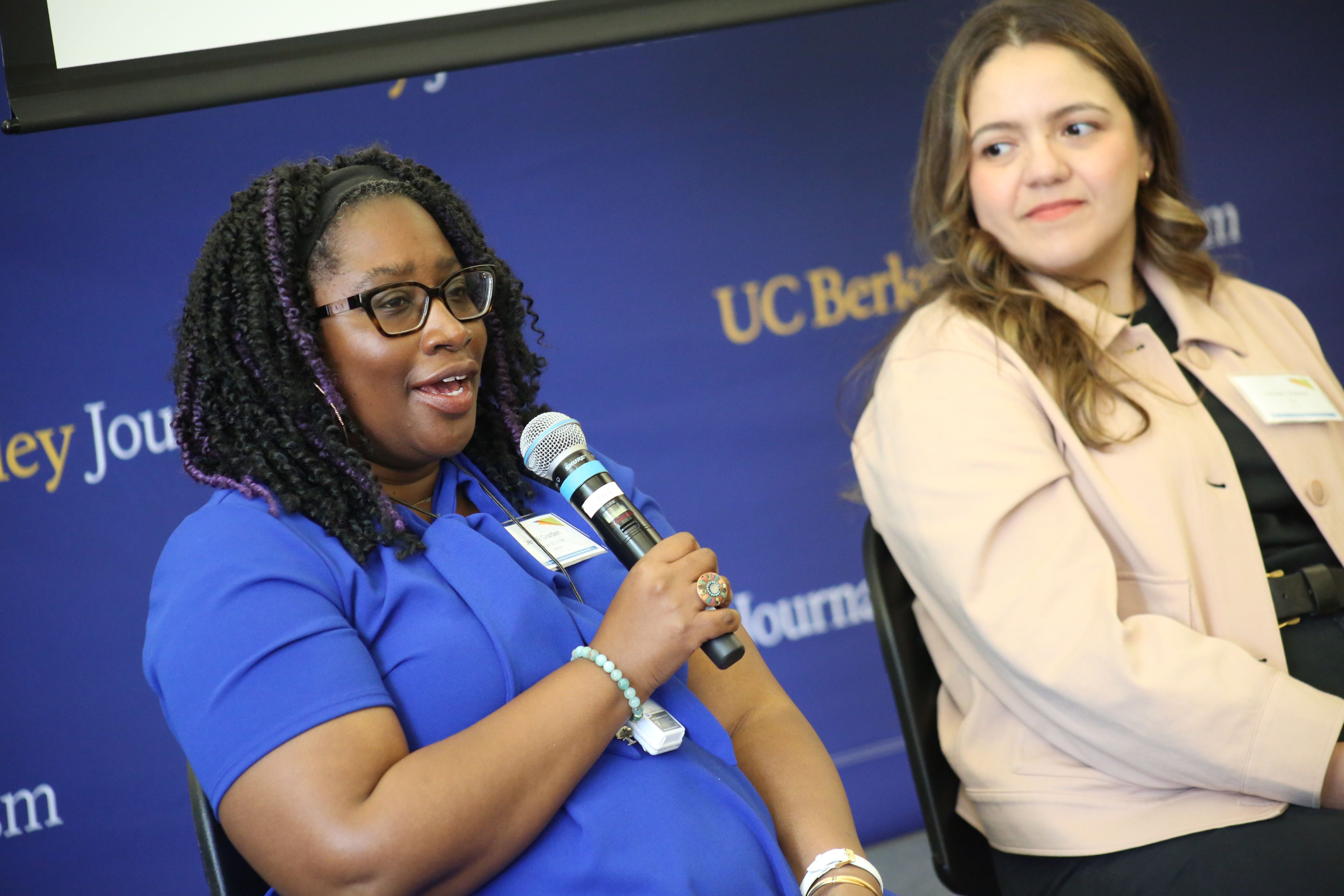 two women on discussion panel and woman in blue shirt is speaking into the microphone