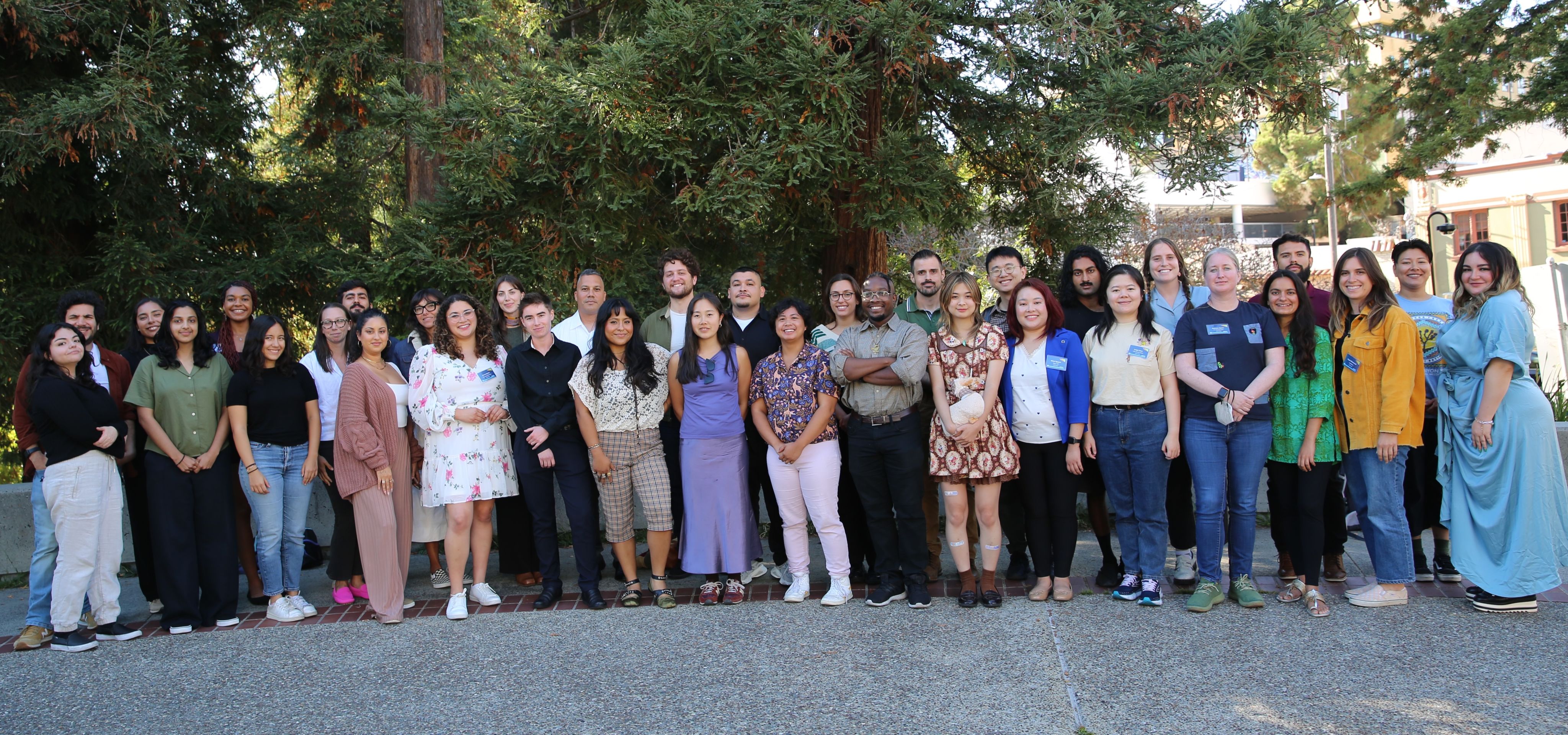A group of people stands two lines in front of trees. 