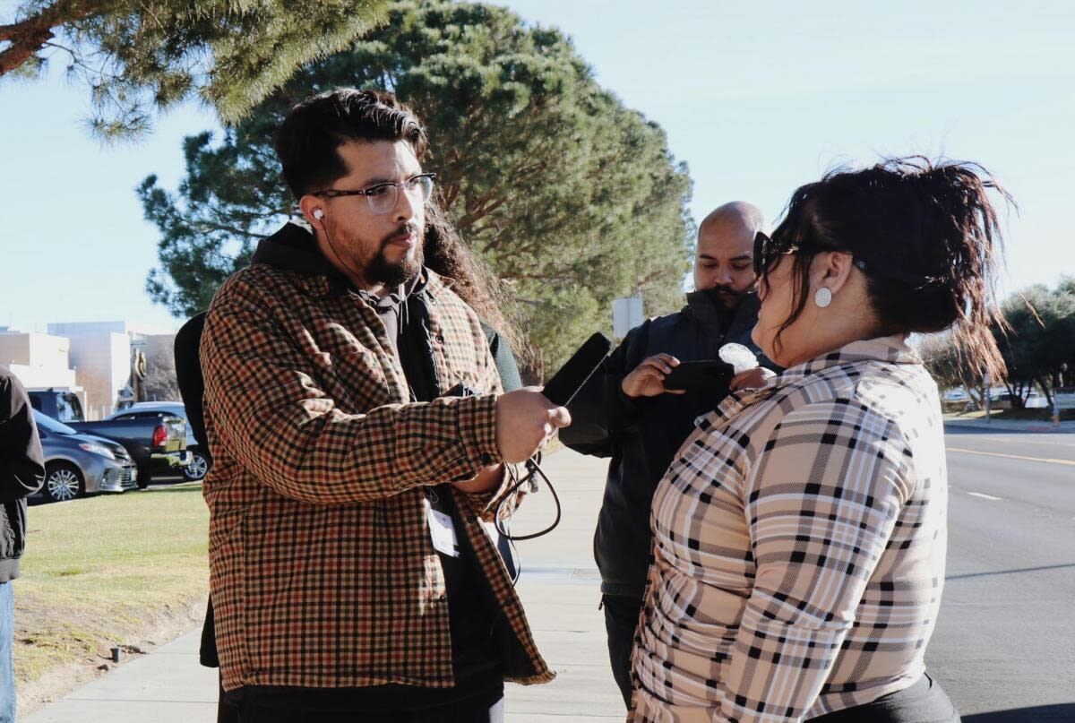 A man with a mic interviews a woman as another man films.
