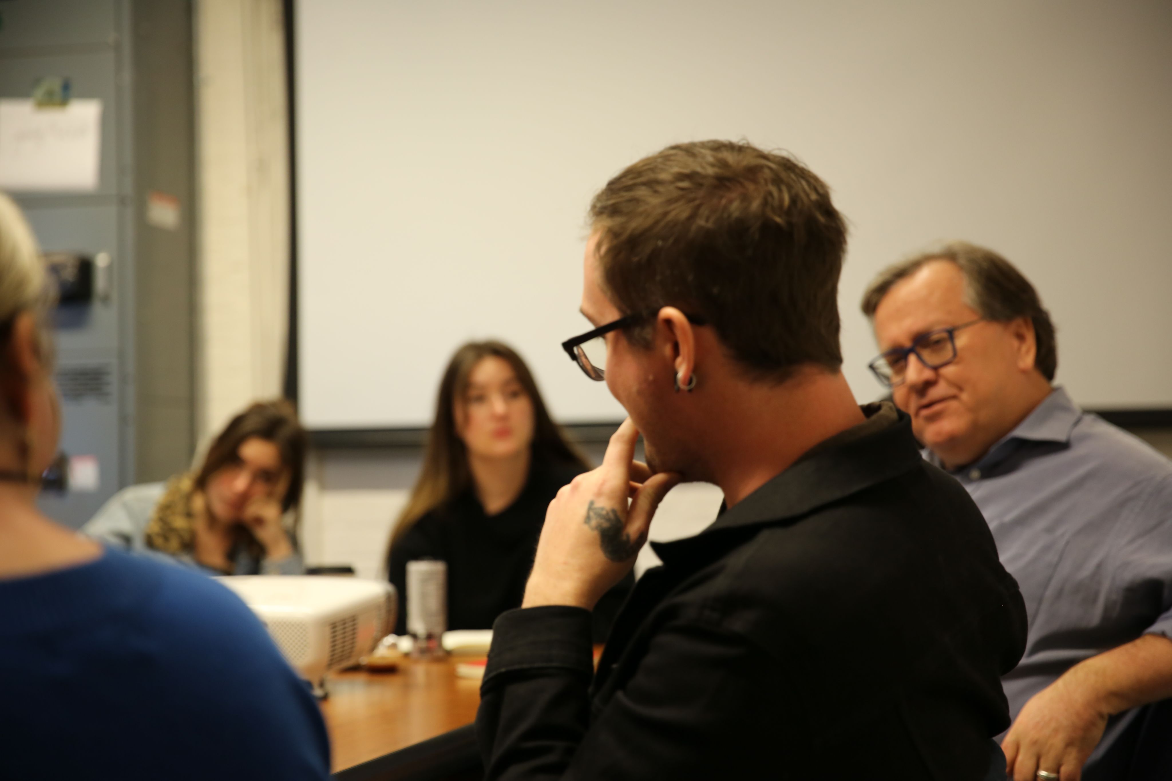 A man with his back to the camera speaks to others in a seminar room. 