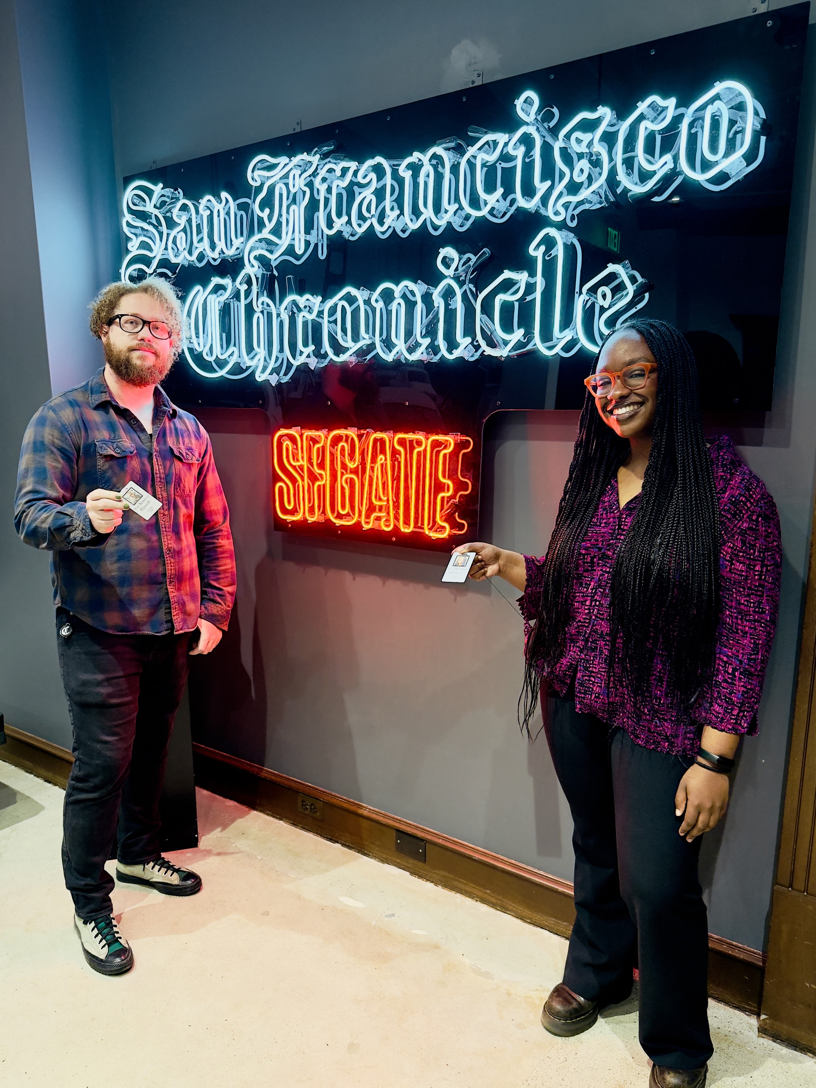 Richard H. Grant and Skylla Mumana stand in front of a neon sign that reads San Francisco Chronicle and SFGate.