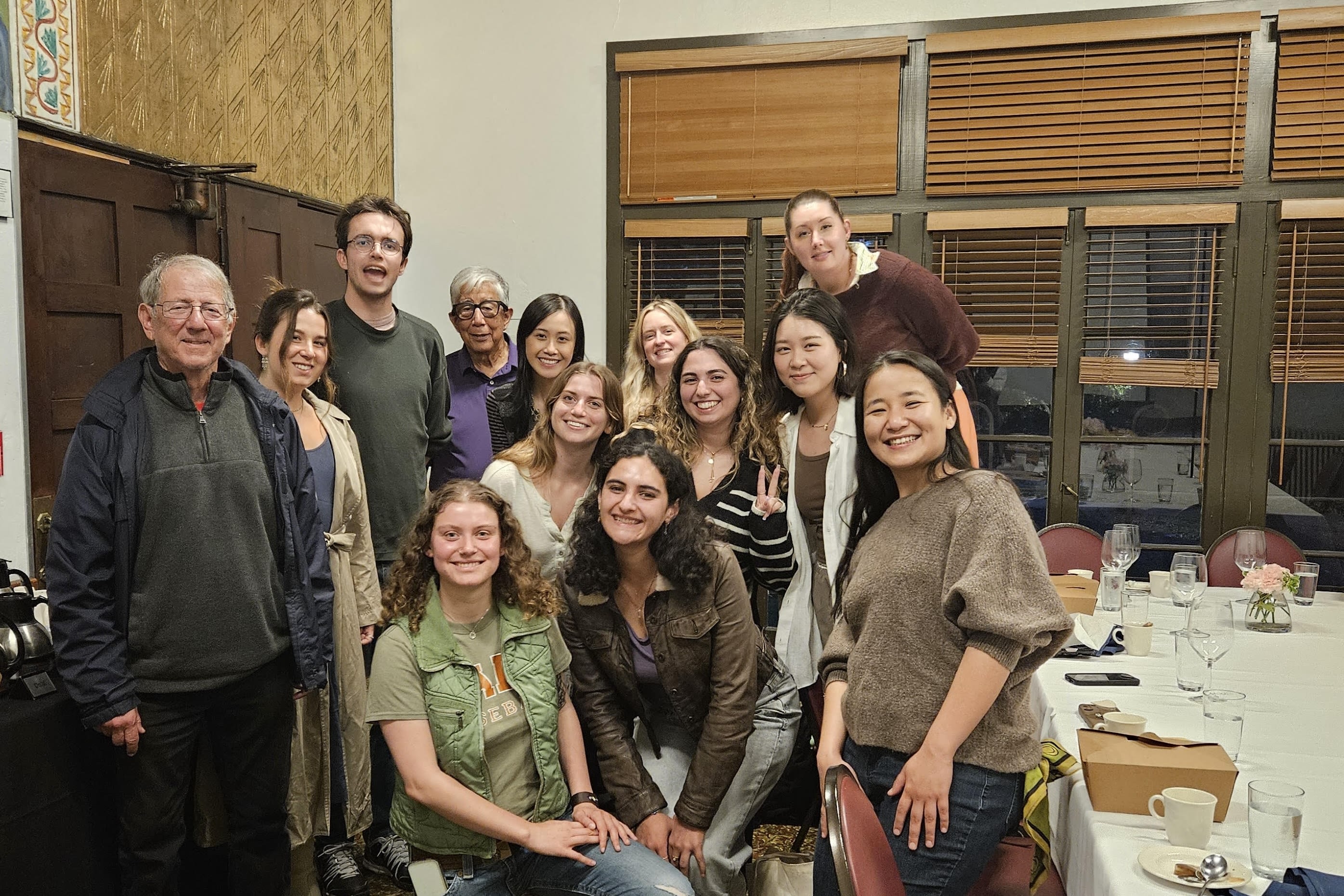 A group of students surround Professor Bill Drummond at a restaurant. 