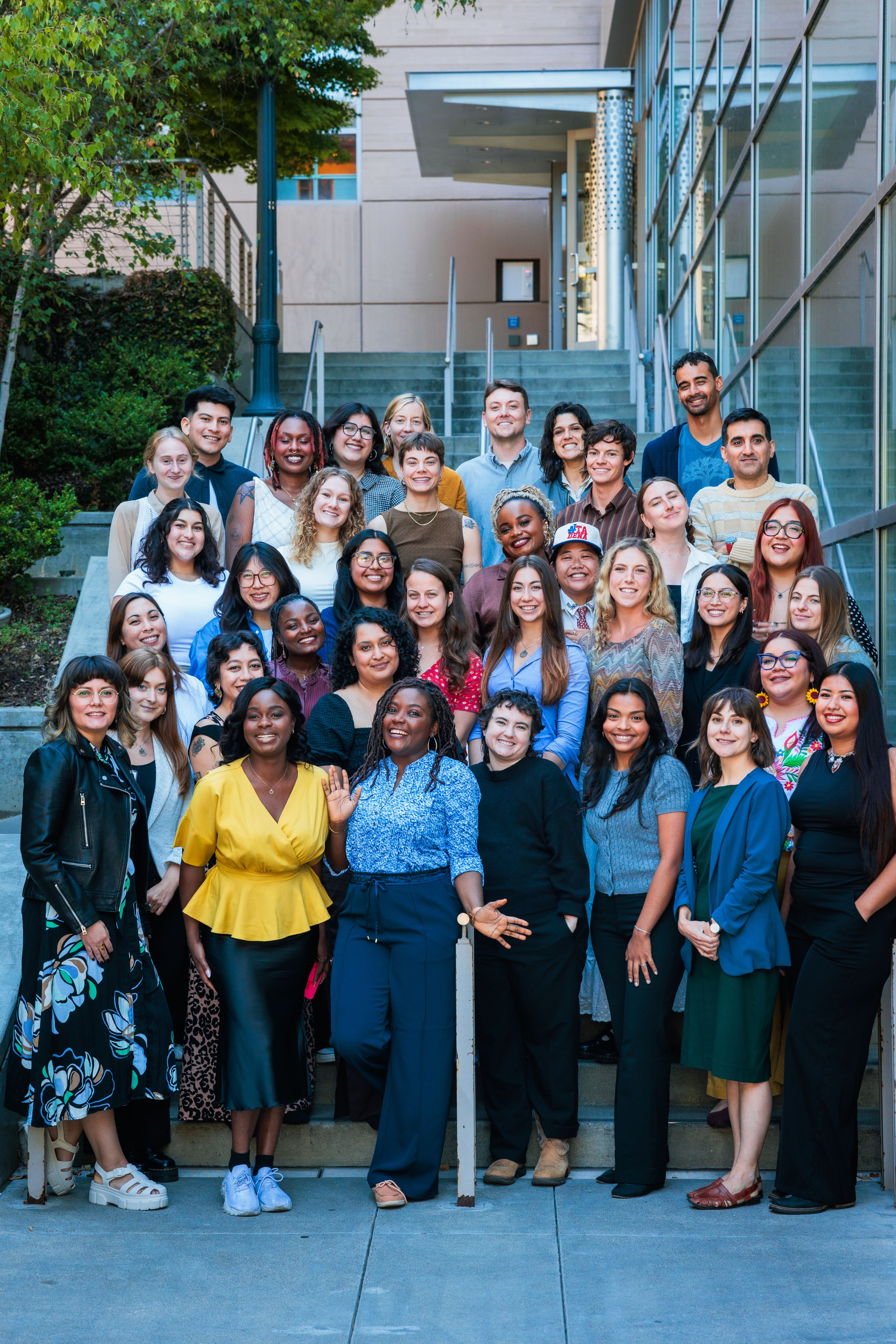 A group of people in colorful clothing pose for a photo. They are the 2025 California Local News Fellows. 