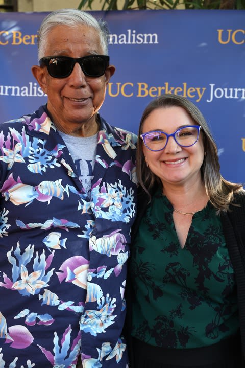 Bill Drummond wears a Hawaiian shirt and is posing with Tamara Keith. Both are smiling. Bill Drummond is wearing dark glasses.